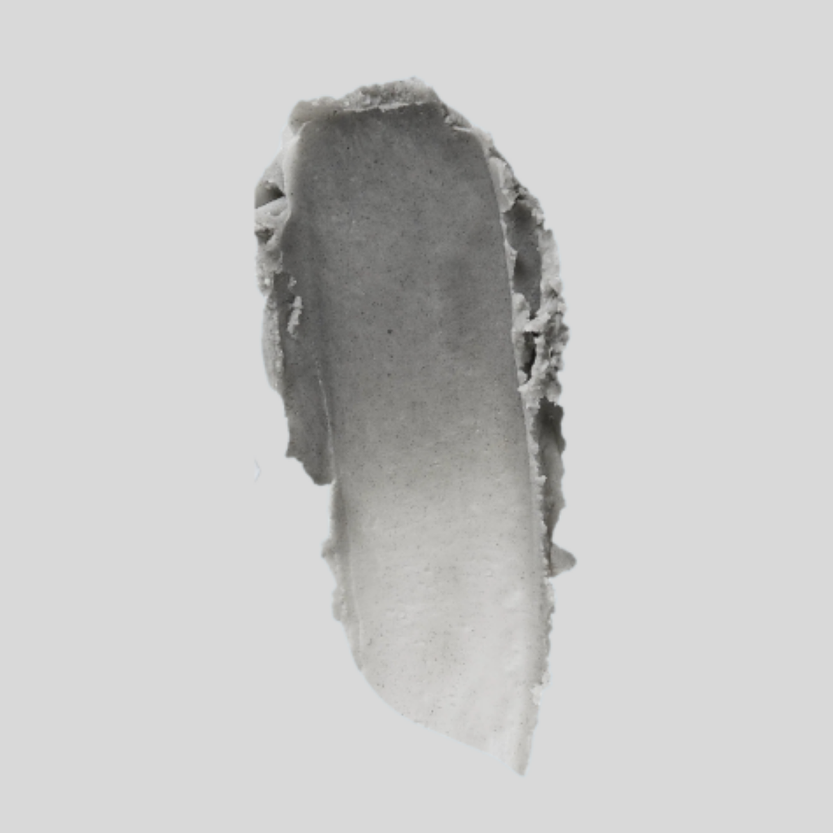 A textured, irregularly shaped gray cosmetic smear or swatch on a solid light gray background.