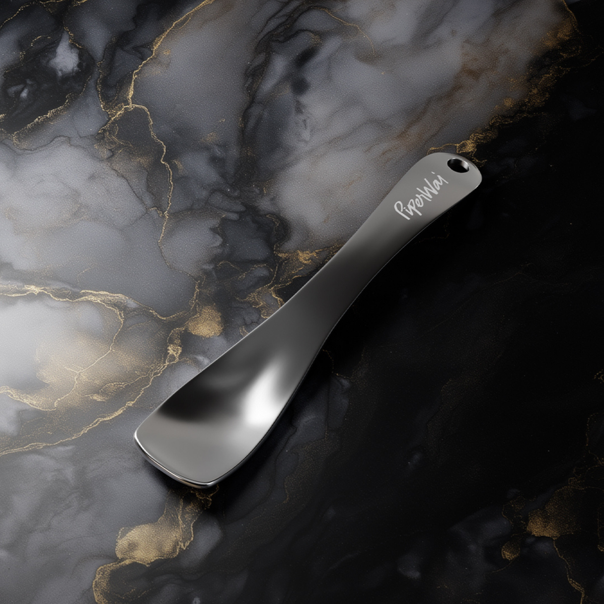 Metal cosmetic spoon with 'PiperWai' branding on a marble background. 