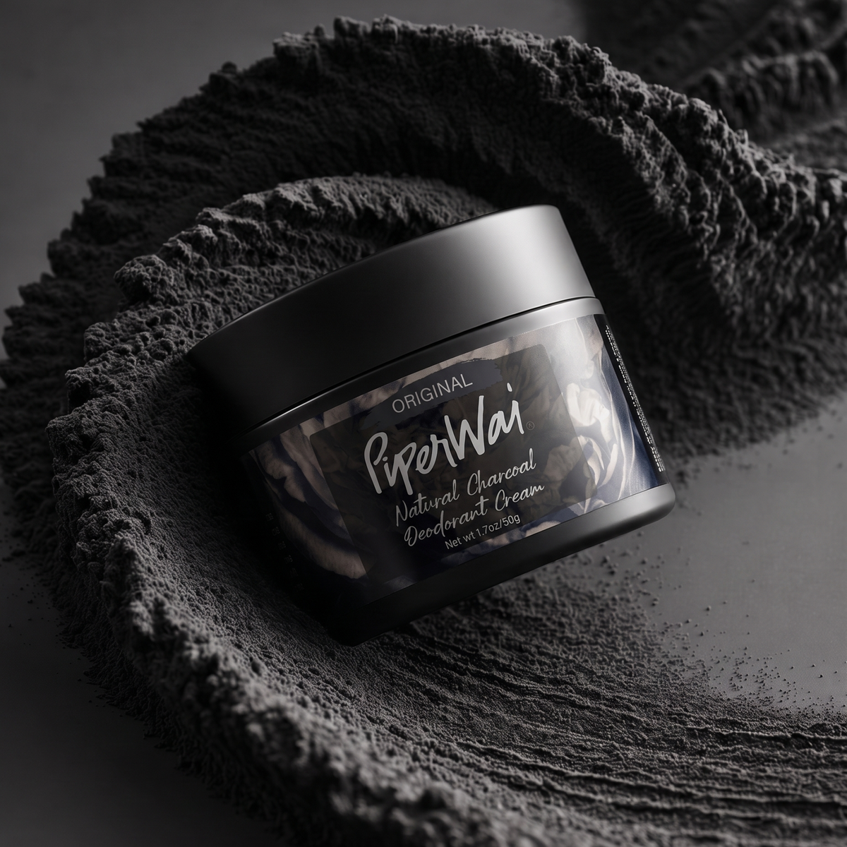 A black jar of PiperWai Original Natural Charcoal Deodorant Cream, styled on a dark textured surface with a matching dark gray towel.

